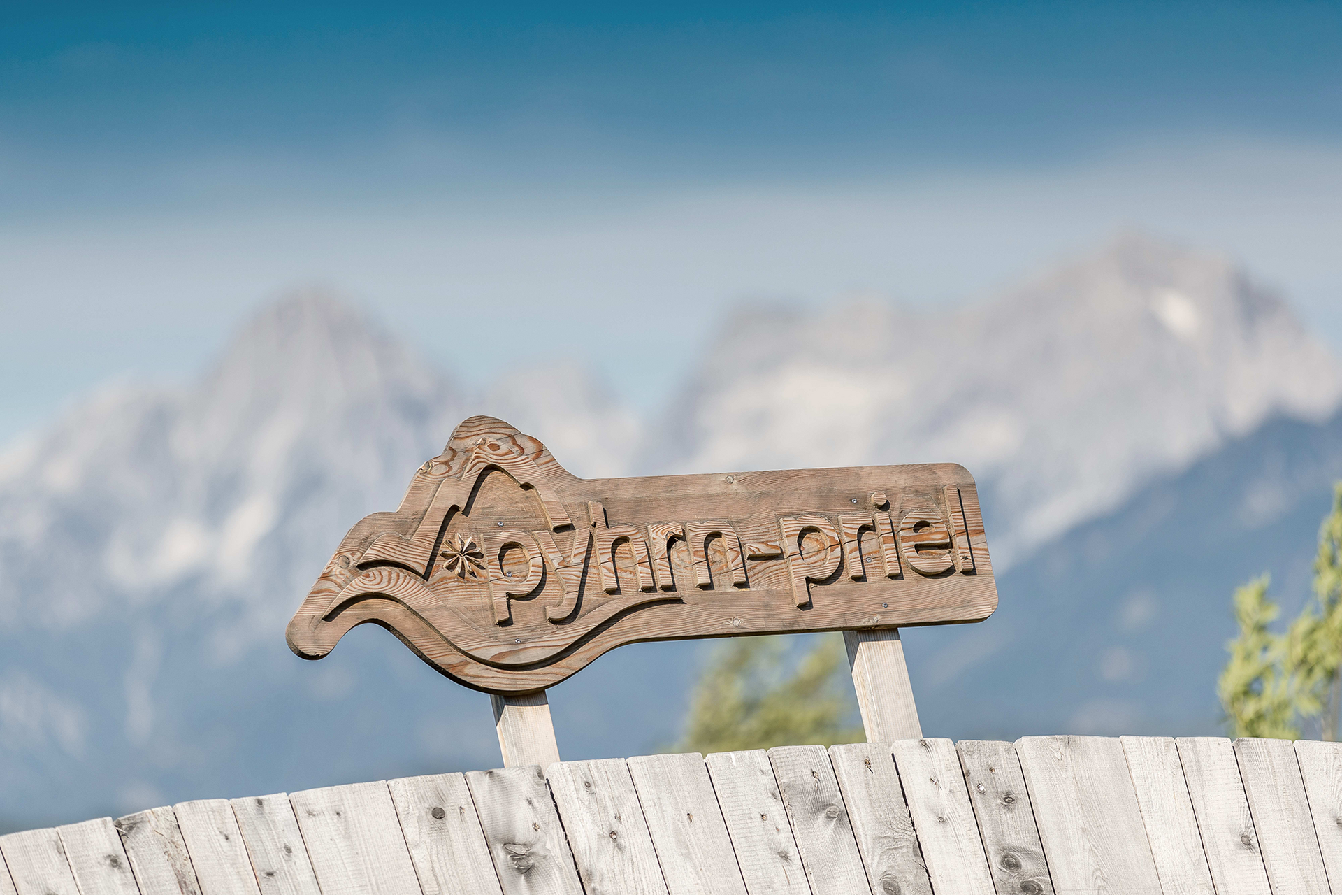 Ausflugstipp Wurbauerkogel Holzschild mit Bergmotiv vor alpiner Berglandschaft.
