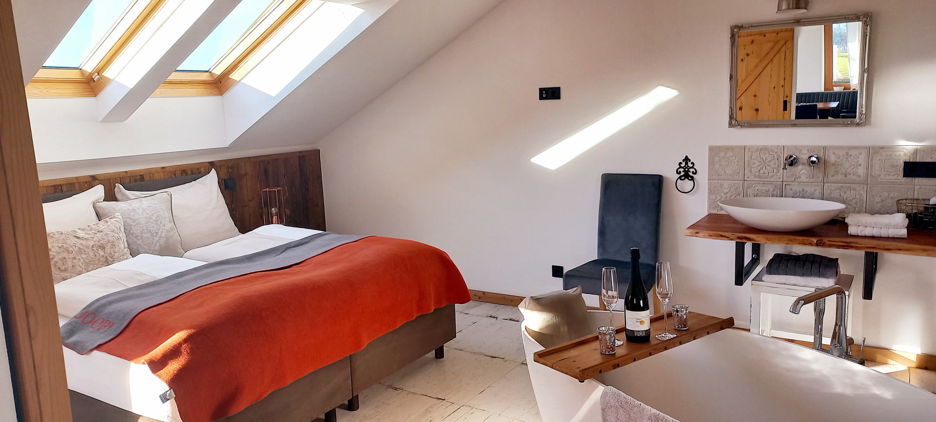Dachgeschoss-Zimmer mit großem Bett, Dachfenstern und Badbereich mit freistehender Badewanne und Weinservice.