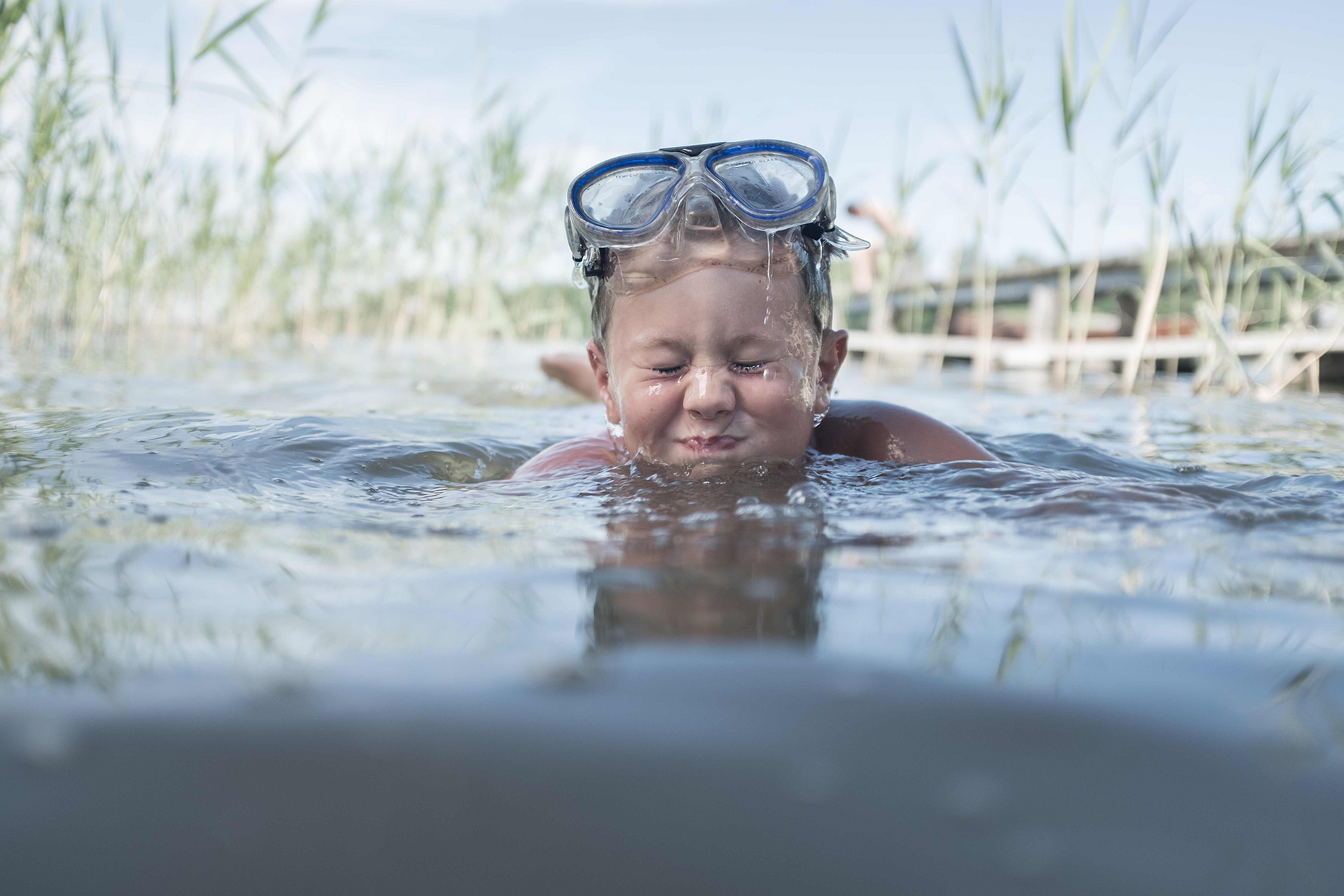 Ein Kind schwimmt im Wasser, trägt Taucherbrille auf dem Kopf, Augen geschlossen.