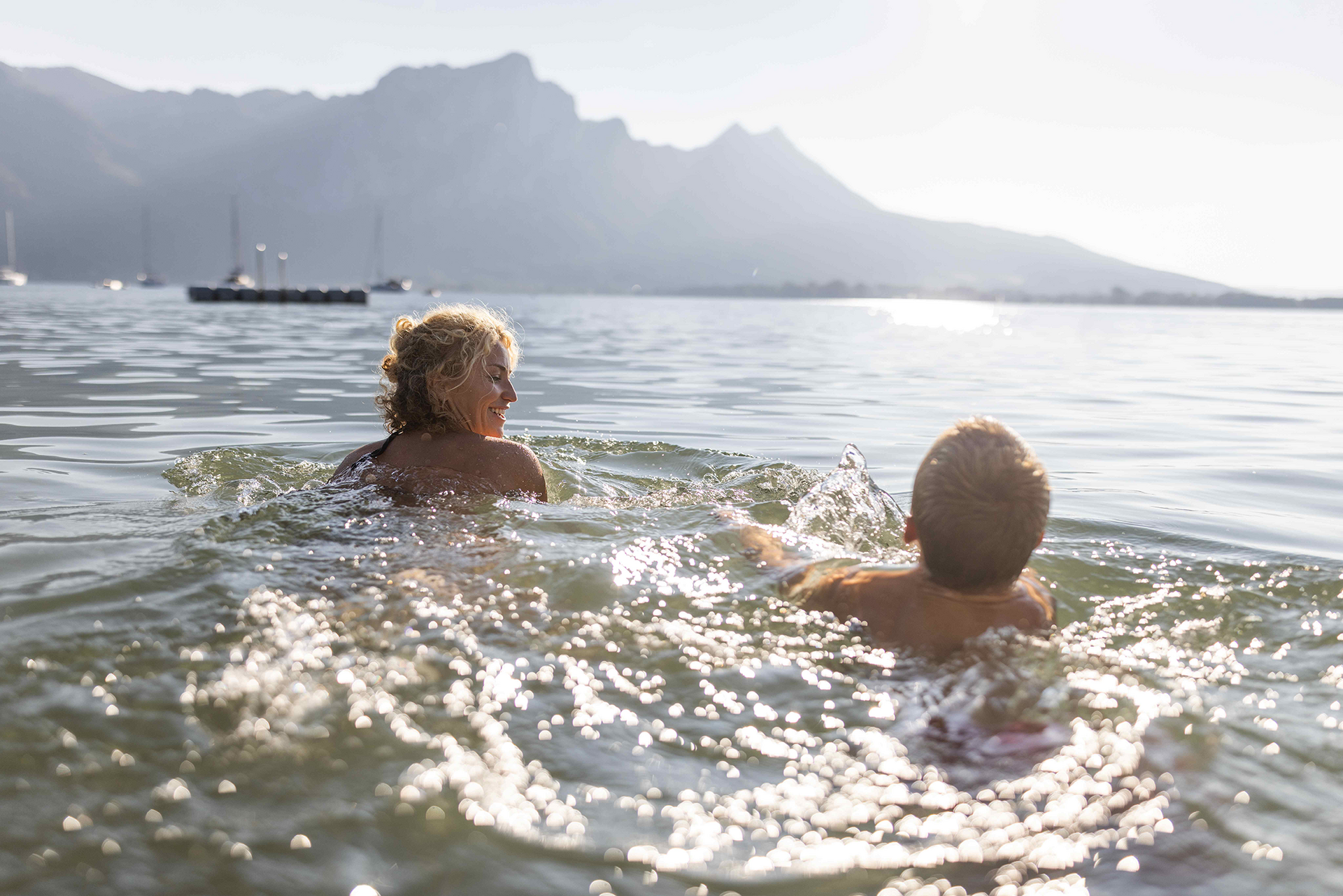 Zwei Schwimmer genießen fröhlich das Seewasser vor einer Bergkette.