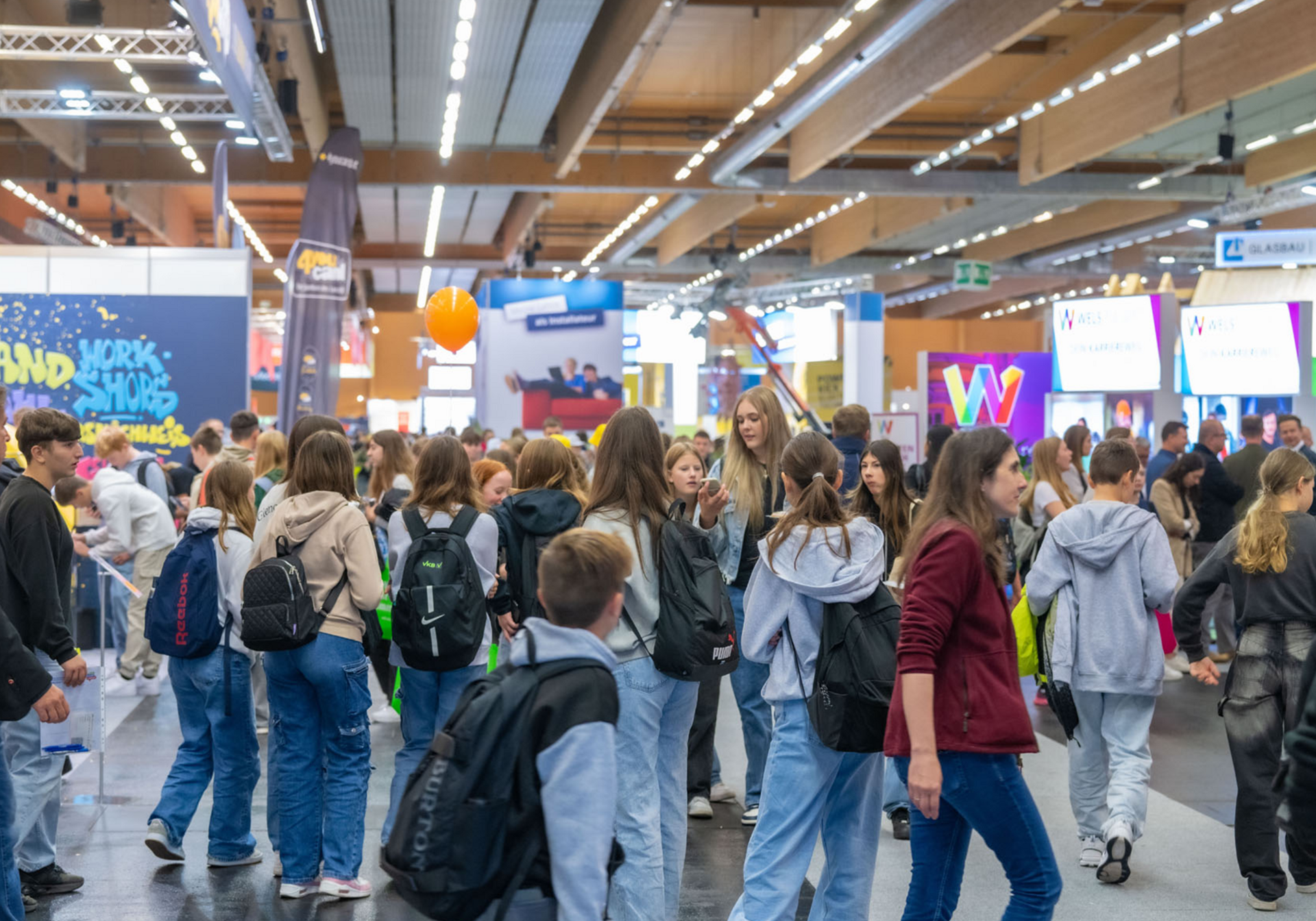 Viele Besucher erkunden eine belebte Messehalle mit Ständen und bunten Bannern.