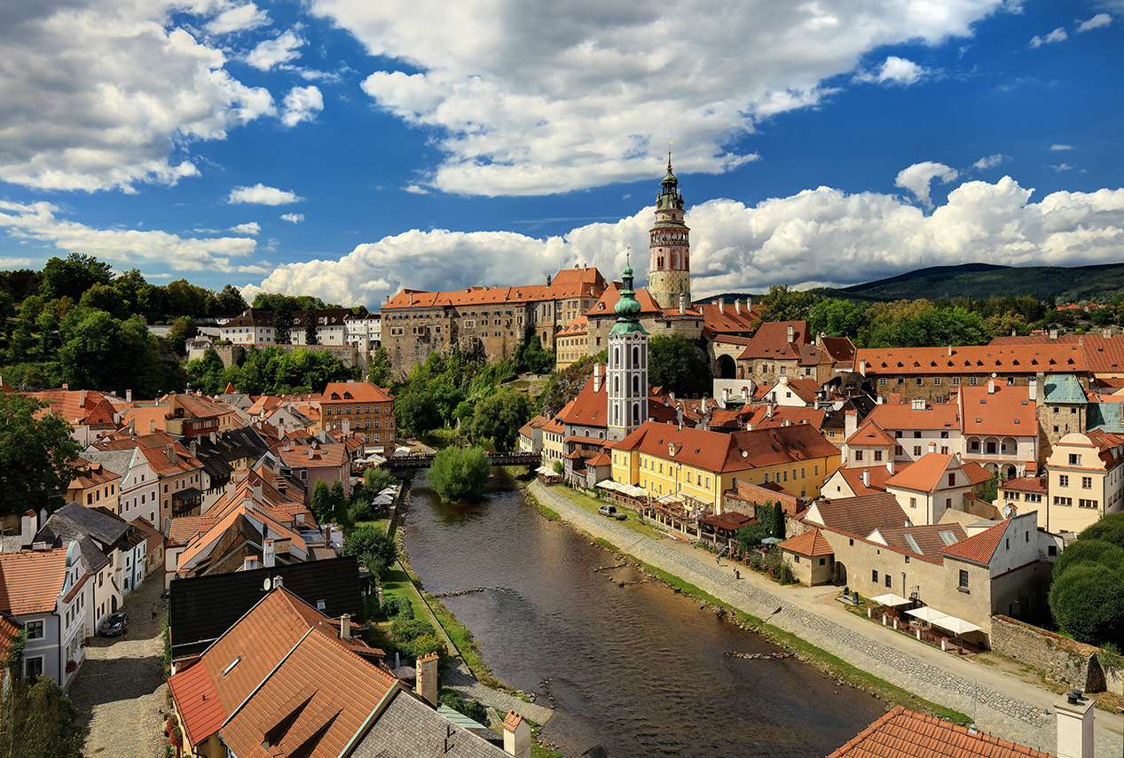 Die Stadt Krumau an der Moldau mit roten Dächern, Kirchturm und Schloss auf dem Hügel.