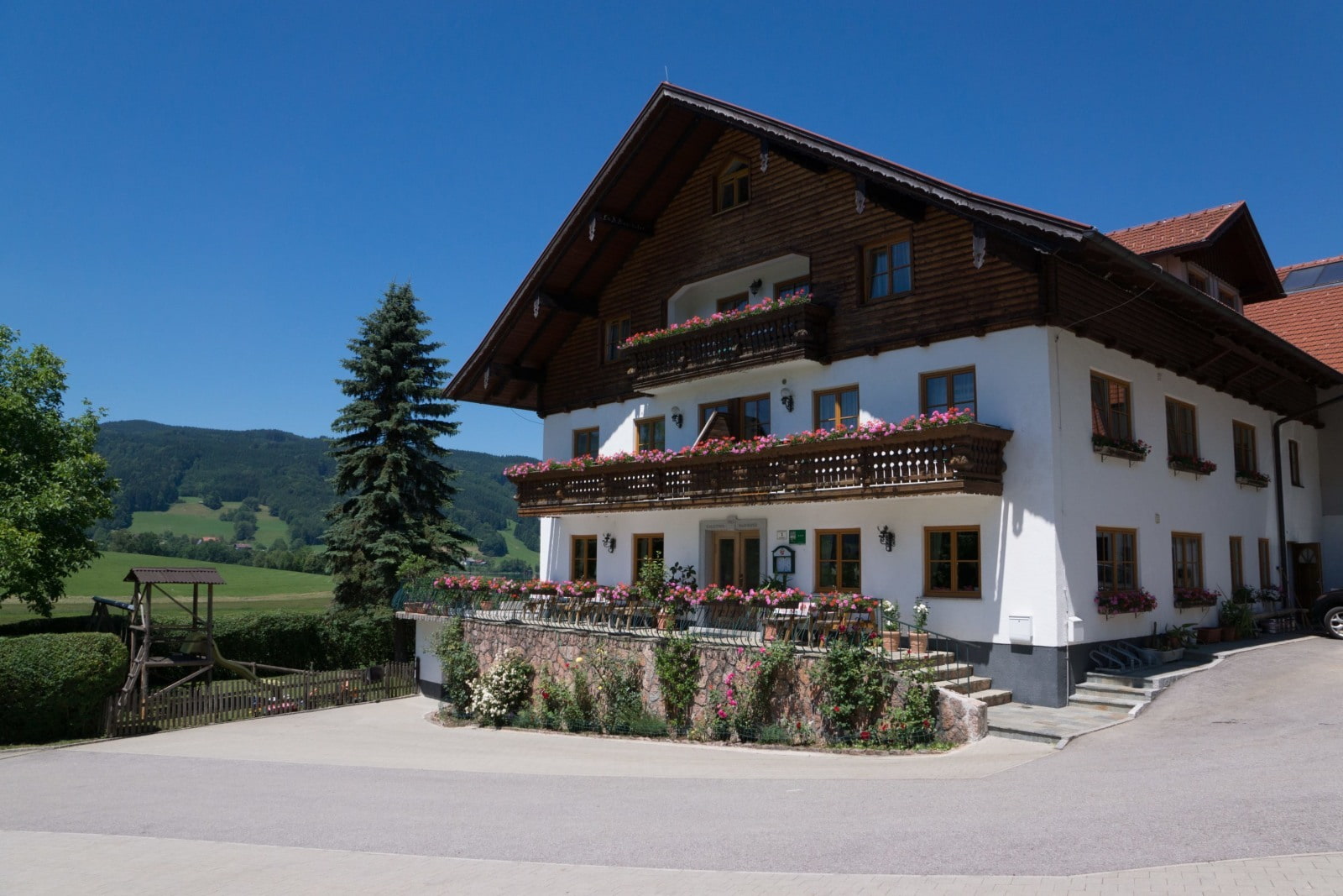 Alpines Gasthaus im Chalet-Stil mit Holzfassade und Balkonblumen vor grüner Landschaft und blauem Himmel.