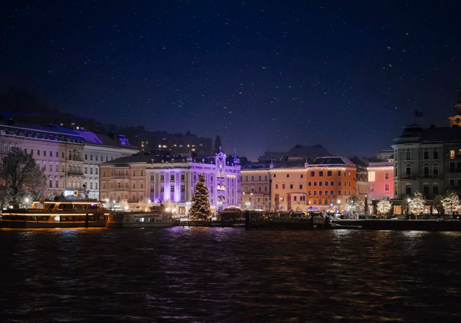 Bild vom Traunsee auf den Stadtplatz von Gmunden mit dem Weihnachtsmarkt bei Nacht.