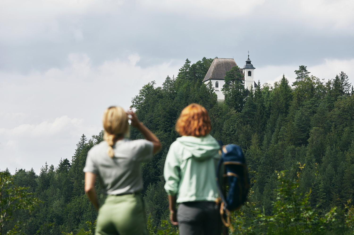 Ausflugstipp Nationalparkregion Sebaldusweg Zwei Wanderer betrachten eine weiße Kirche auf einem Waldhügel.