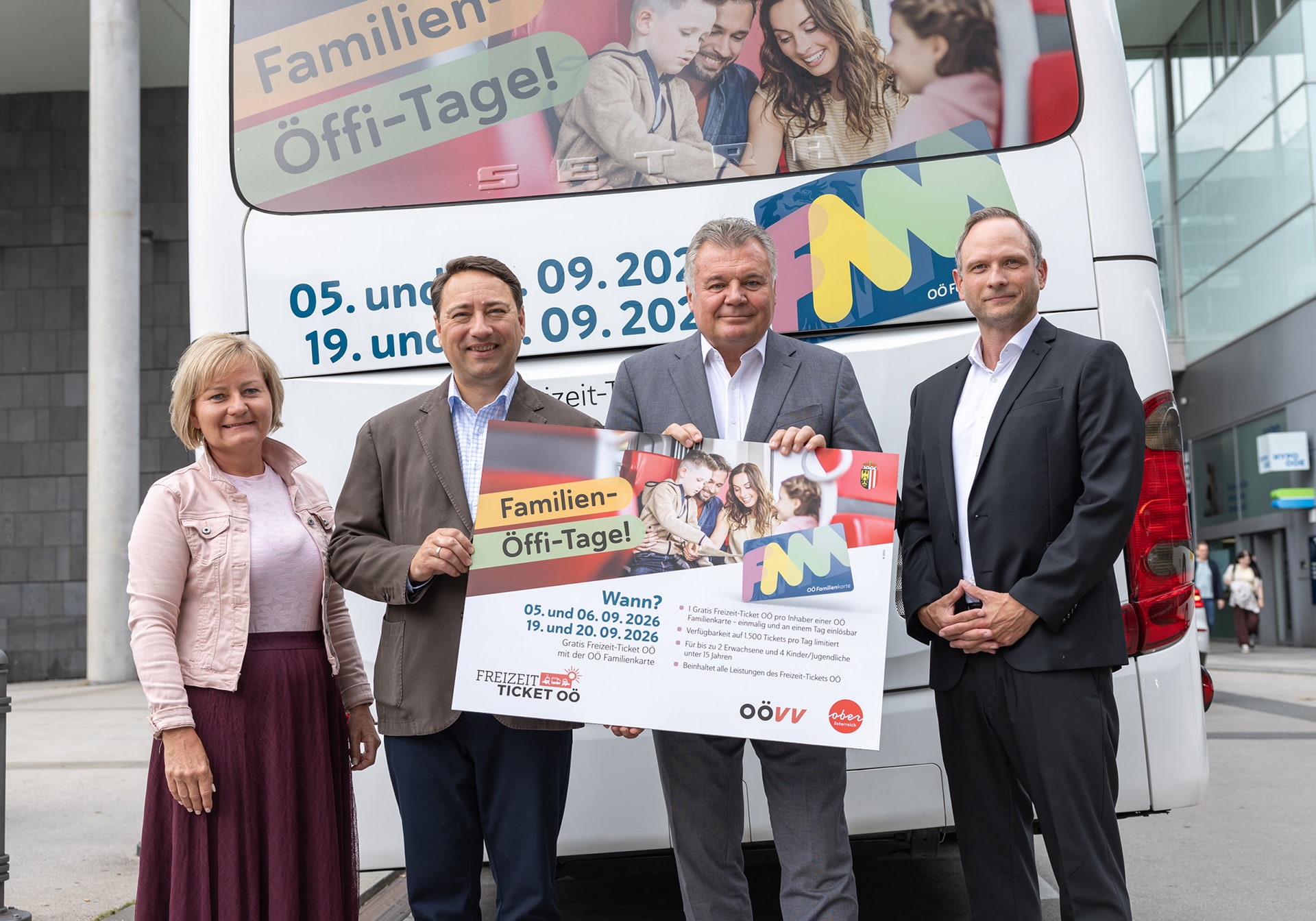 Three people hold up an advertising poster in front of a bus promoting Family-Öffi Days.