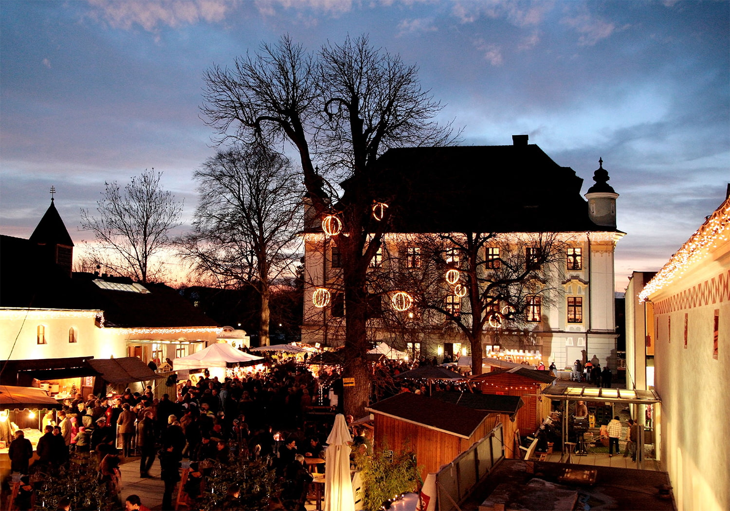 Schloss Traun inklusive Weihnachtsmarkt bei Nacht mit winterlicher Beleuchtung.